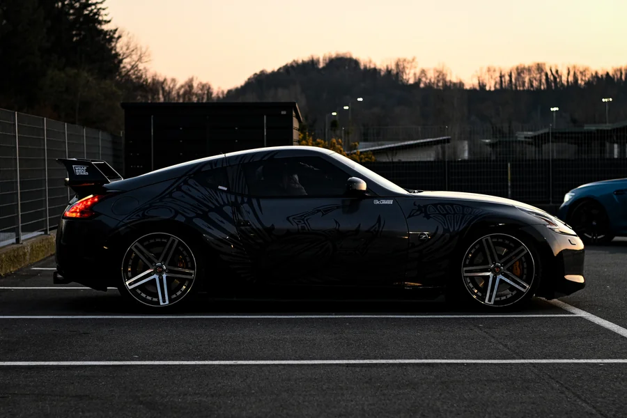 Il profilo di una coupé scura in un parcheggio, con il cielo del tramonto sullo sfondo.