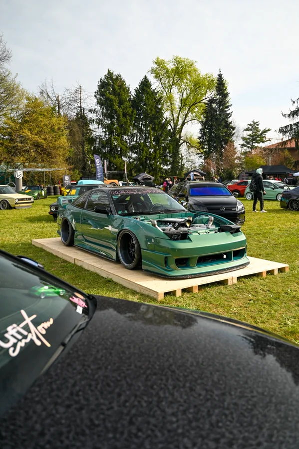 Una vettura verde personalizzata esposta su una pedana durante un raduno all’aperto.