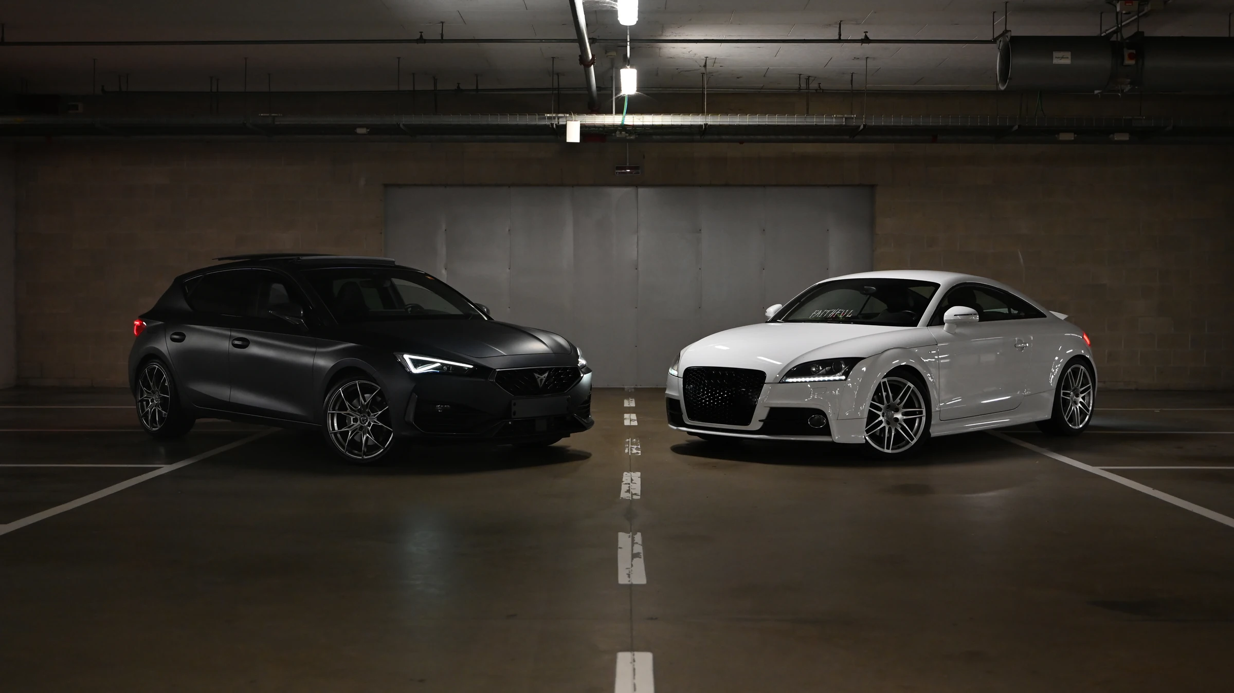 Due auto sportive, una scura e una bianca, in un parcheggio sotterraneo.